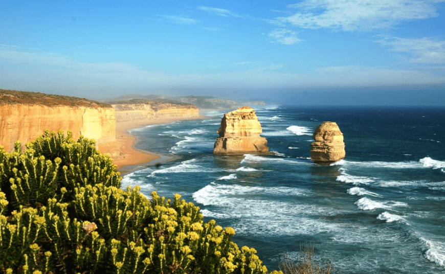 The ocean waves and cliffside with unique foliage at Twelve Apostles in Victoria, Australia under a clear blue sky which is a great place to move internationally.