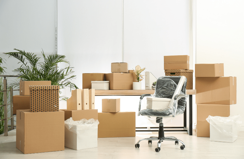 An employee's office surrounded by packing boxes around a desk covered in more boxes and a house plant with a plastic-wrapped desk chair in front ready for an international move.
