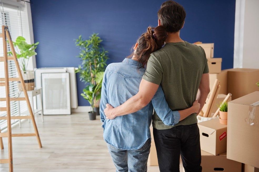 A couple standing in their newly packed up living room hugging as they move house after a job was offered to one of them with the opportunity to relocate abroad