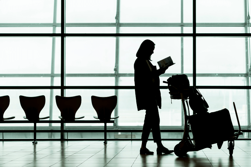 A woman reading by her luggage in an airport ready to board her flight after hiring a removal company for a cost-efficient relocation.