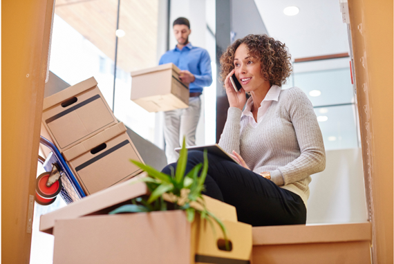 A woman, taking a break from packing boxes, sits on her stairs telling her family about her relocating to another country